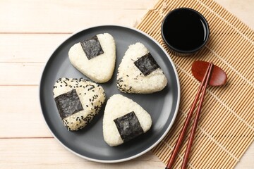 Rice balls (onigiri), soy sauce and chopsticks on wooden table, flat lay. Traditional Japanese dish