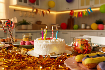 Tasty cake with burning candles and different treats on table indoors. Birthday surprise party