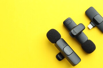 Lavalier microphones and wireless receiver on yellow background, flat lay. Space for text