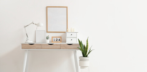 Modern table with stylish desk lamp, calendar and candles near white wall