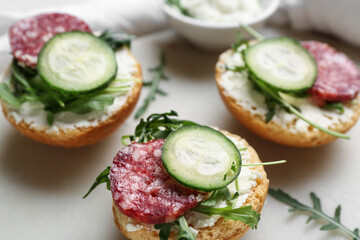 Tasty sandwiches with cream cheese, salami and cucumber on board, closeup