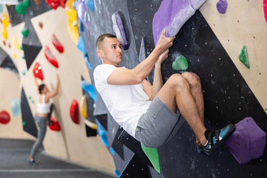 Male visitor to fitness club clambs wall for amateur climbers, side view. Active recreation, hobbies, recreation for active and sporty people