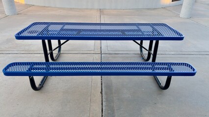 empty metal picnic table sits near closed concession stand in quiet sports park shadows stretch across concrete ground breeze moves litter nearby silent pause between games and gatherings