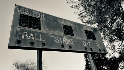 faded wooden scoreboard with peeling paint classic numbers rusted metal frame vintage team logos ivy creeping along edges nostalgic summer sky in background timeless charm of old baseball days
