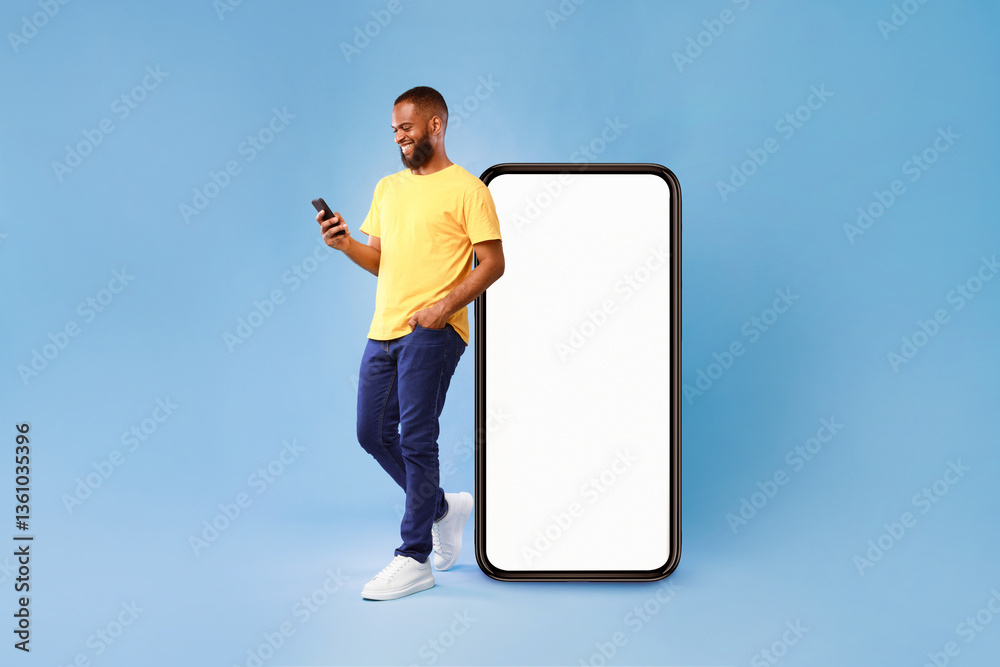 Leinwandbilder handsome young african american man using mobile phone while standing near huge smartphone with empt