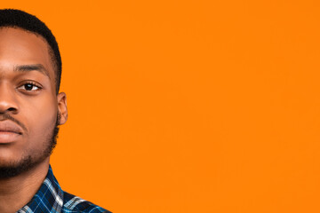 Half-Face Portrait Of African American Man Looking At Camera With Serious Face Expression Posing On Yellow Studio Background. Copy Space