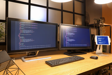Fototapeta premium programmer's desk with computer monitors and tablet in dark office at night