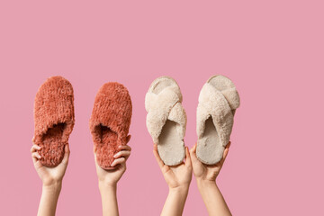 Female hands holding fluffy woman's slippers on pink background
