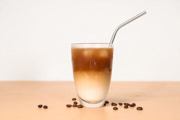 Glass of iced latte and coffee beans on beige table