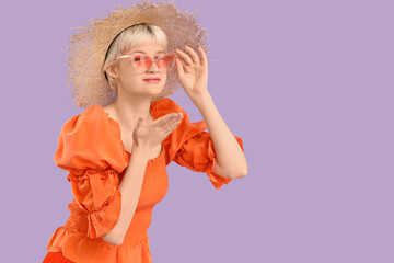 Portrait of beautiful young woman with sunglasses blowing kiss on lilac background