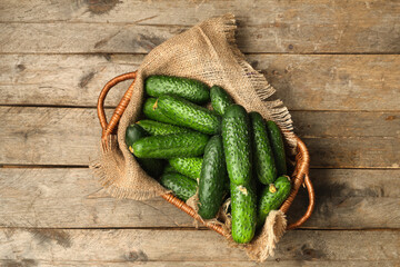 Wicker basket with fresh green cucumbers on wooden background