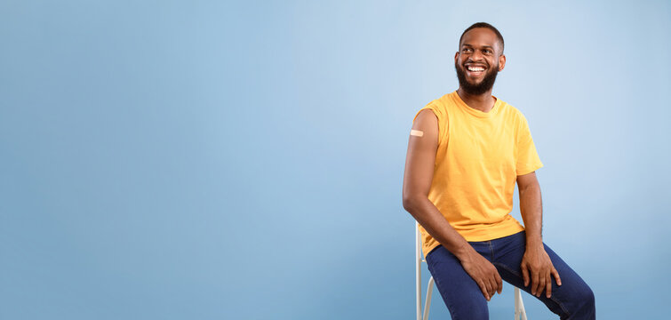 Flu immunization. Joyful vaccinated African American guy showing shoulder with band aid plaster after anti flu vaccine shot, receiving vaccination on blue studio background, copy space