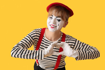 Female pantomimist making heart with her hands on yellow background
