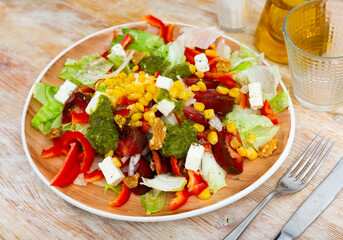 Appetizing salad of fresh vegetables served with feta cheese and pesto on plate