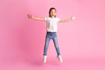 Cheerful little asian girl jumping isolated over pink studio wall. Full length, copy space, vertical photo