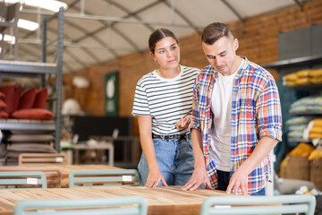 Obraz premium Positive young couple, girl and guy inspecting outdoor furniture at home and garden store, choosing patio table and enjoying time together