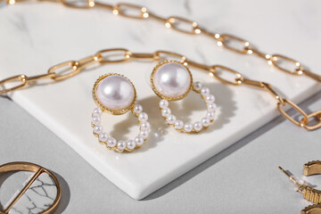 Board with beautiful earrings and golden chain necklace on grey background
