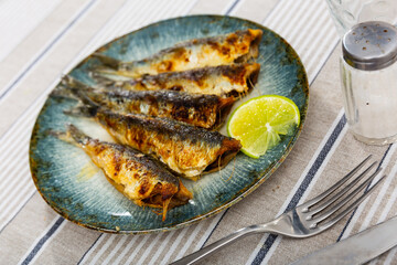 Five perfectly grilled sardines, golden and crisp, served on ceramic plate with wedge of refreshing lime for Mediterranean styled meal