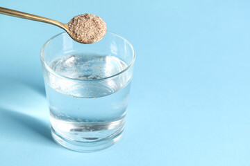 Glass of water and spoon with psyllium husk on light blue background