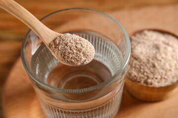 Glass of water and spoon with psyllium husk on table, closeup
