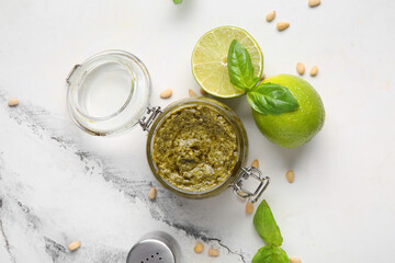 Jar of delicious pesto sauce with ingredients on marble background