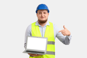 Young male engineer with laptop on light background