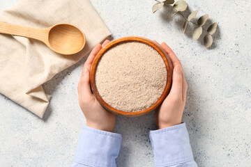 Female hands and bowl with psyllium husk powder on light background