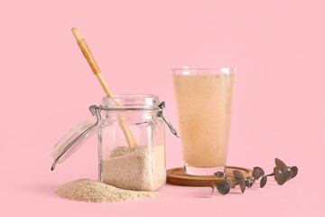 Jar with psyllium husk powder and glass of water on pink background
