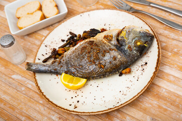 Appetizing grilled dorada fish served with vegetable garnish of roasted Brussels sprouts, green beans, peas, chickpeas and fresh lemon slice