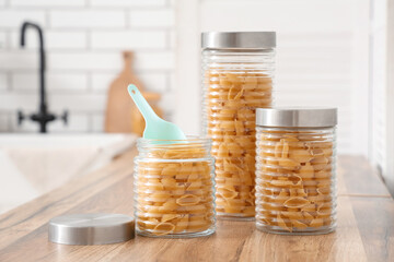 Different jars with raw pasta shells on table in kitchen