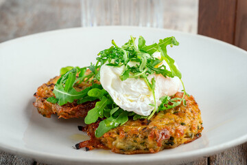 Potato patties with poached egg and arugula on a white plate. Breakfast with Hash browns and egg