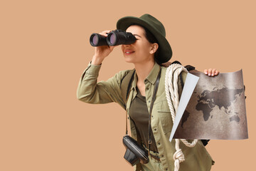 Young female tourist with map looking through binoculars on beige background