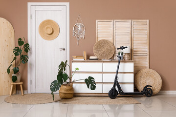 Interior of living room with electric scooter, commode, houseplants and folding screen near brown...