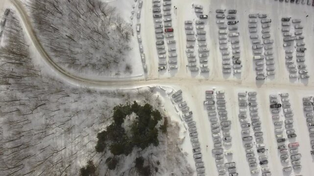 Top dowm aerial view capturing a winding road meandering through snowy parking lots and a serene forest in Orford, Quebec, Canada, on a cloudy winter day, and the tranquil beauty of the landscape