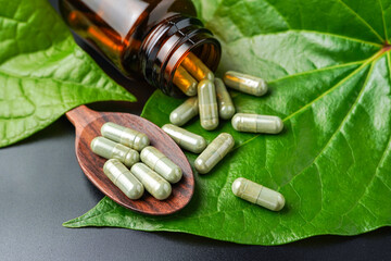 Pile of herbal capsules on wooden spoon with herbs and green natural Betel pepper leaf background