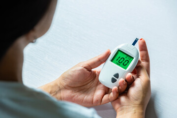 Woman's hands checking diabetes and hyperglycemia with digital blood sugar meter. Healthcare and...