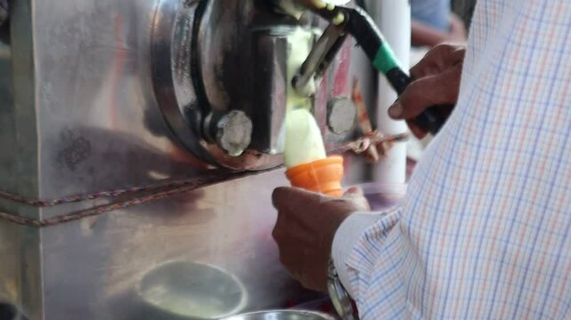 An Indian street vendor crafts softy ice cream in a crunchy cone, topped with colorful fruit cubes, blending creamy sweetness with fresh, vibrant flavors