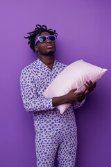 Sleepy person in pajamas holding a pillow on a purple background.
