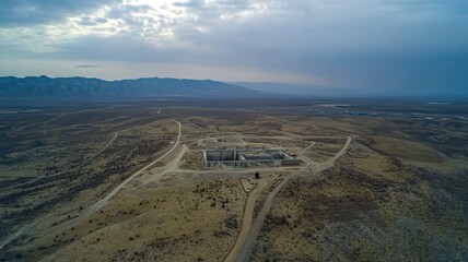 Aerial view of secure nuclear waste storage facility with warning signs and containment structures in barren landscape under cloudy sky. Environmental safety and hazardous material management concepts