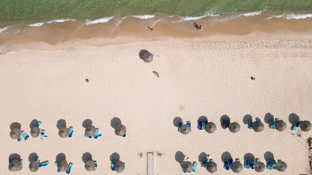 An aerial view of a neatly arranged beach setup with rows of straw umbrellas and sun loungers. The clean white sand and orderly arrangement provide a tranquil and inviting environment for visitors.