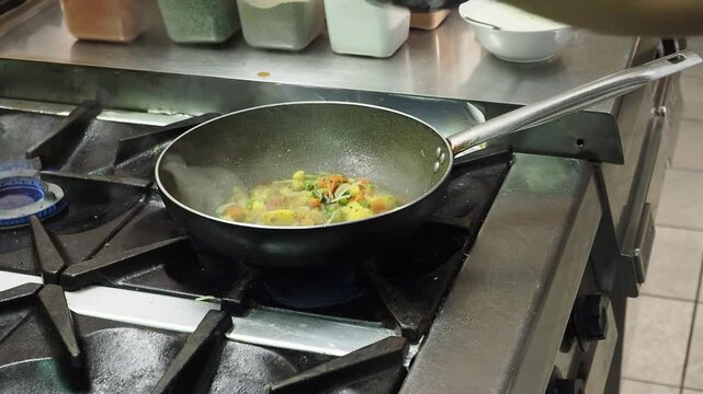 Professional chef meticulously preparing authentic Indian cuisine, carefully adding basmati rice to sizzling pan with onios and aromatic spices in bustling commercial kitchen environment