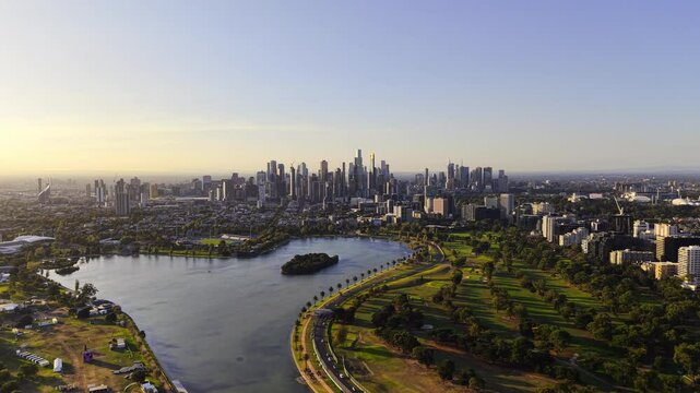 Drone video from above Albert Park in Melbourne flying toward the city with the sun starting to set on the left of the video