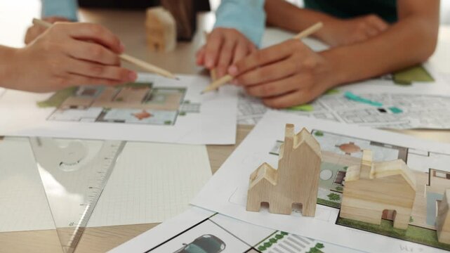 Smart architect and safety engineer discussion about building blueprint on table with architectural document, measurement tools and wooden block scatter around at modern office. Closeup. Delineation.