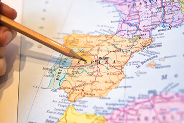 Hand pointing at Spain on a map with a wooden pencil, highlighting travel planning