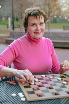The woman makes a move with her checker and smiles