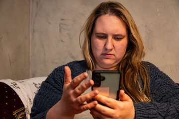 Fototapeta premium Mother engaged with smartphone while seated comfortably at home in cozy surroundings