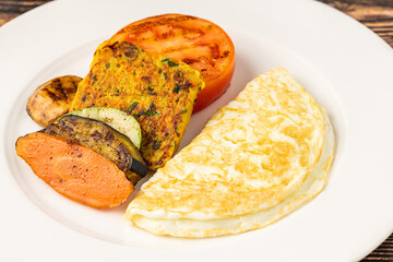 Rustic breakfast plate with fried eggs, grilled vegetables, and turkey bacon