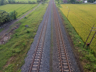 Symmetrical aerial view of dual railway tracks over gravel and surrounded by grassy terrain.