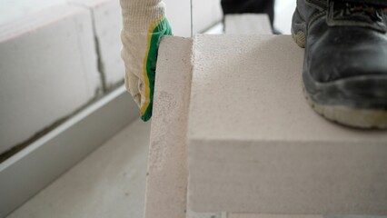 Construction worker cutting aerated concrete block with hand saw, preparing it for laying on the wall