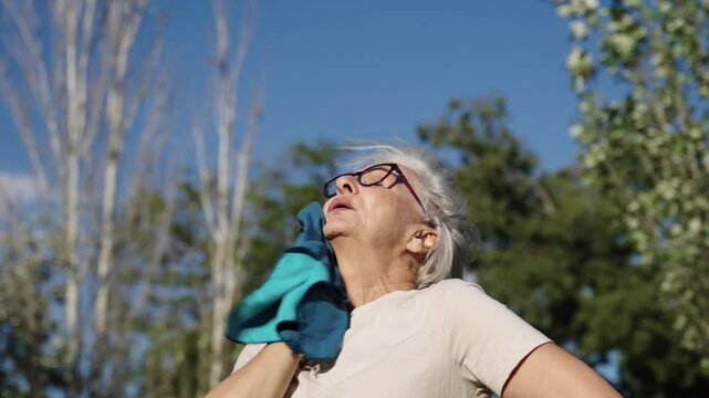 Senior woman wipes sweat from her forehead in slow motion